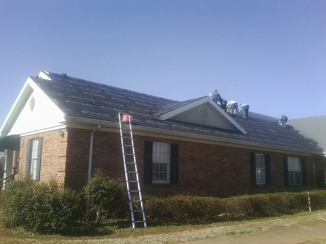 Crew tearing shingles off a brick ranch roof with a ladder set — Emergency Roof Repair work by our crew in Tolland