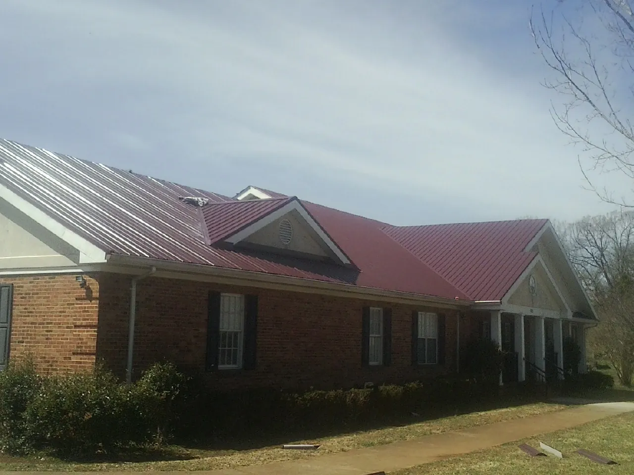Red metal roof with gabled entries on a long brick building, from a Hail Damage Roof Repair job in Tolland