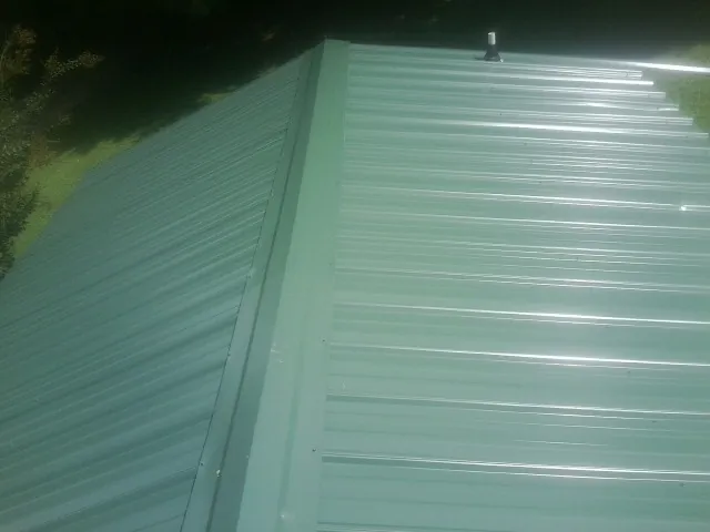 New green metal panels meeting at the ridge of a roof — Flat Roof Repair work by our crew in Tolland