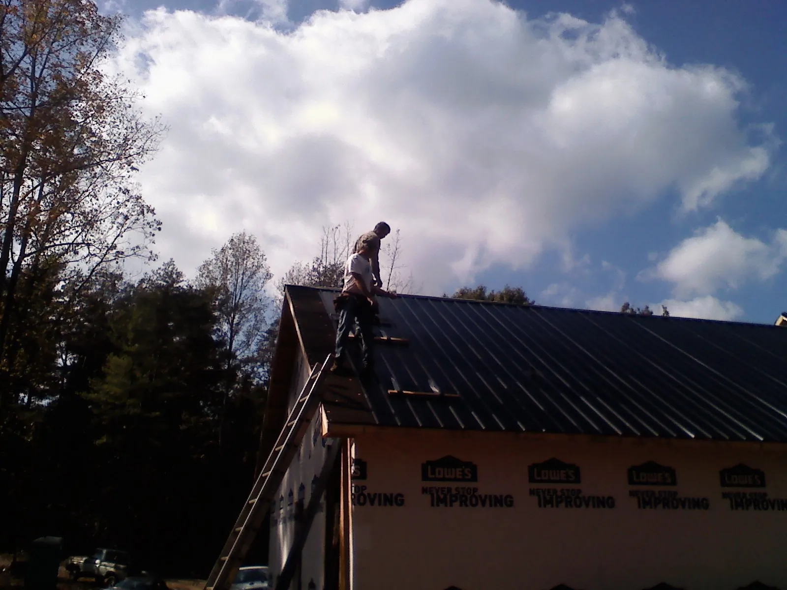 Roofer fastening dark metal panels high against a cloudy sky, from a Roof Inspection job in Tolland