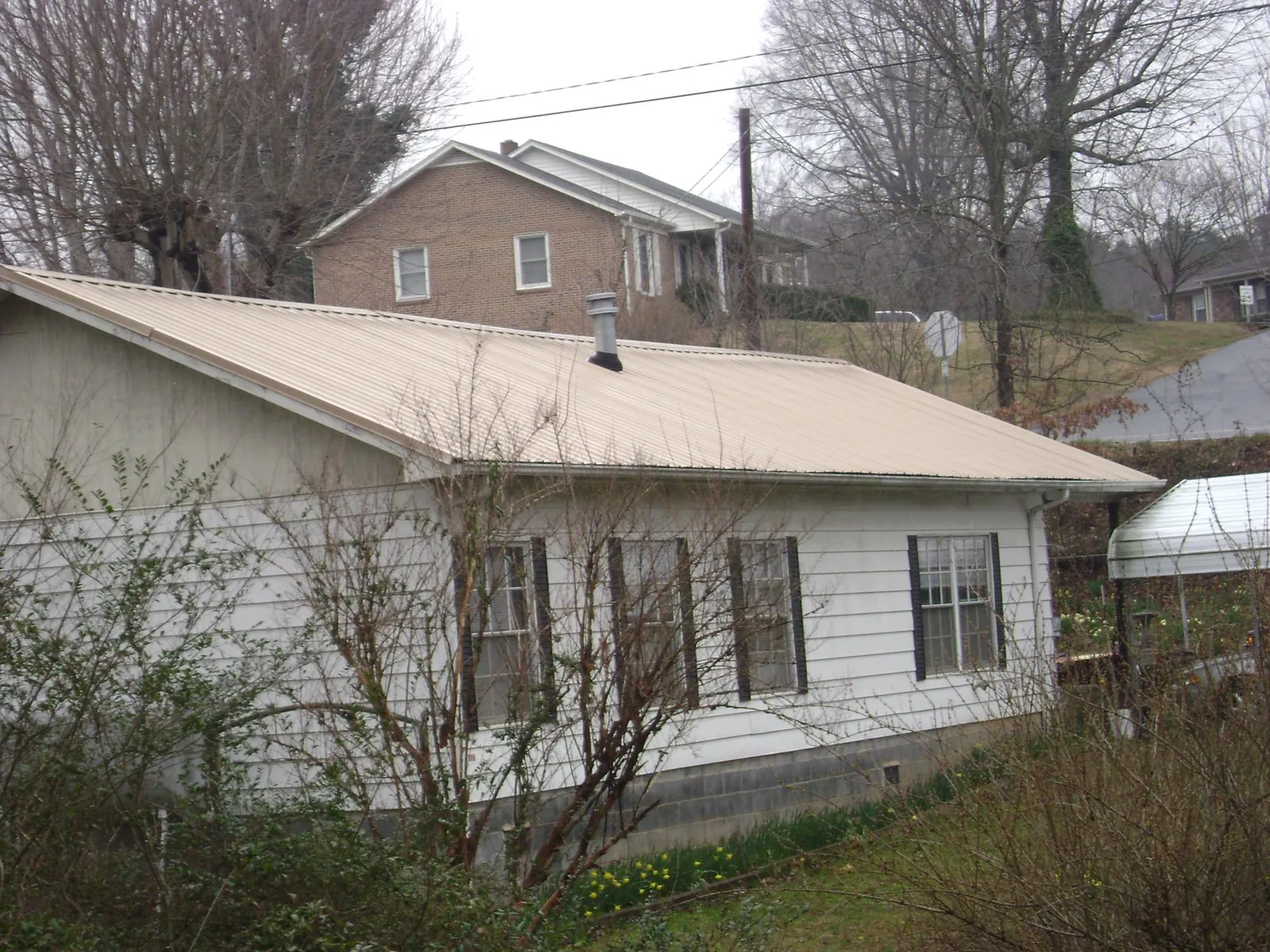 Tan metal roof on a white sided house set into a hillside — Commercial Roofing by Roofing Brothers in Tolland